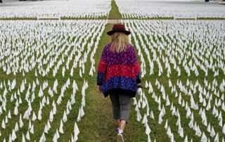 In this Oct. 27, 2020, file photo, Artist Suzanne Brennan Firstenberg walks among thousands of white flags planted in remembrance of Americans who have died of COVID-19 near Robert F. Kennedy Memorial Stadium in Washington. Firstenberg's temporary art installation, called "In America, How Could This Happen," will include an estimated 240,000 flags when completed.